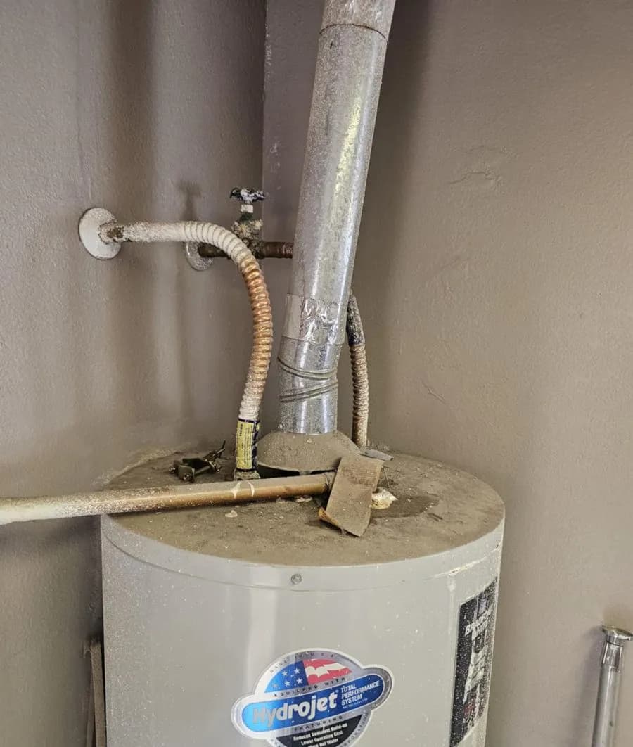 An aging gas water heater with corroded flex connectors and vent piping, photographed on a service call