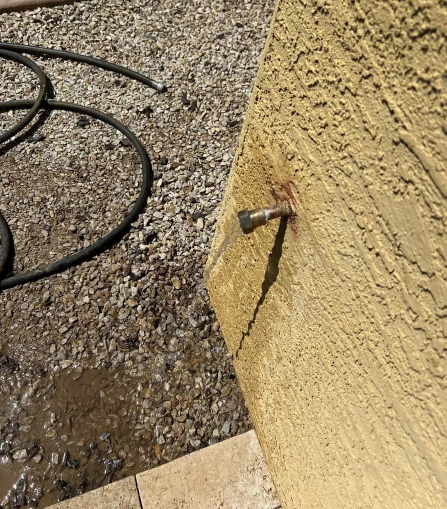 Water pooling in gravel beneath a leaking exterior hose bib on a stucco wall